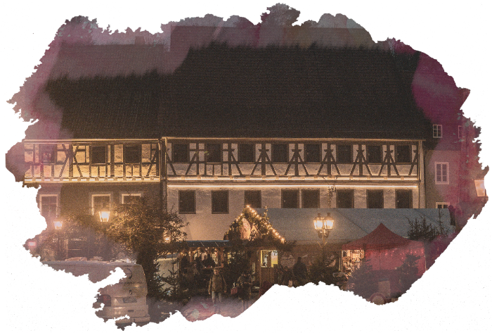black and white half timbered house at night with lit huts of the market below